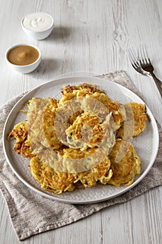 Homemade Potato Pancakes Latkes with Apple Sauce and Sour Cream on a white wooden background, side view
