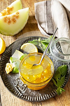 Homemade preserve. Sweet melon and citrus jam or jelly in small glass jar with fresh melon slices on wooden rustic table