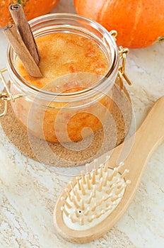 Homemade pumpkin face mask (scrub) in a glass jar and wooden hairbrush. Natural autumn beauty treatment and spa