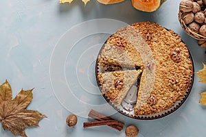 Homemade pumpkin pie with cinnamon and walnuts on a plate, with a slice of the pie cut out, on a light blue background