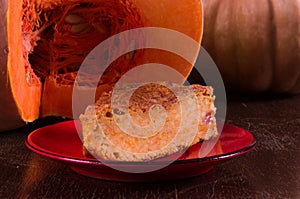Homemade pumpkin pie for Thanksgiving on a red saucer, and a large fresh sliced orange pumpkin, wooden background, close
