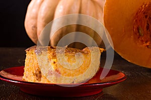 Homemade pumpkin pie for Thanksgiving on a red saucer, and a large fresh sliced orange pumpkin, wooden background, close