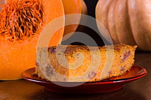 Homemade pumpkin pie for Thanksgiving on a red saucer, and a large fresh sliced orange pumpkin, wooden background, close