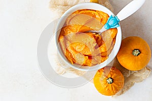 Homemade pumpkin puree in bowl with baby spoon and fresh pumpkins on light concrete background. The concept of baby food