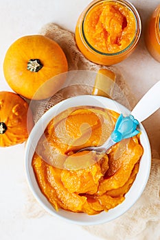 Homemade pumpkin puree in bowl with baby spoon and fresh pumpkins on light concrete background. The concept of baby food