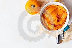 Homemade pumpkin puree in bowl with baby spoon and fresh pumpkins on light concrete background. The concept of baby food. Top view