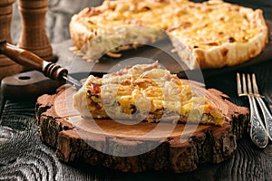 Homemade quiche with leek, ham and cheese on wooden background.