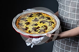 Homemade quiche lorraine in women`s hands with mushrooms, cheese and thyme. A young woman holds a large tart with Mushroom pie on