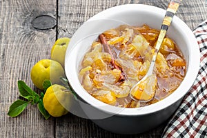 Homemade quince jam in ceramic bowl and fresh quince with leaves on wooden table