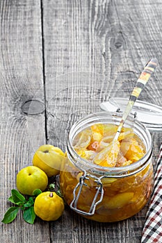 Homemade quince jam in glass jars and fresh quince with leaves on wooden table