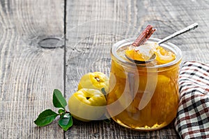 Homemade quince jam in glass jars and fresh quince with leaves on wooden table