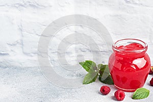 Homemade raspberry jam in a glass jar and fresh raspberries with mint on a grey concrete background. Copy space