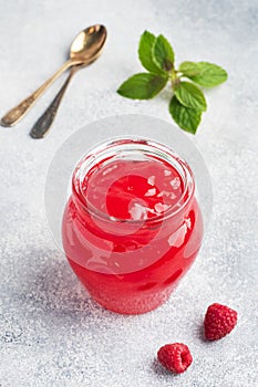 Homemade raspberry jam in a glass jar and fresh raspberries with mint on a grey concrete background. Copy space