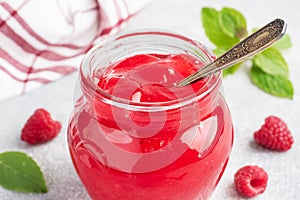 Homemade raspberry jam in a glass jar and fresh raspberries with mint on a grey concrete background. Copy space