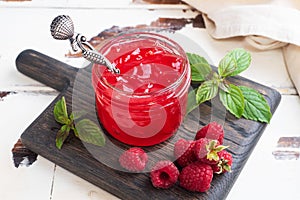 Homemade raspberry jam in a glass jar and fresh raspberries with mint on a wooden rustic background