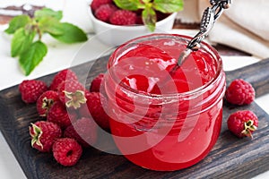 Homemade raspberry jam in a glass jar and fresh raspberries with mint on a wooden rustic background. Close up