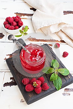 Homemade raspberry jam in a glass jar and fresh raspberries with mint on a wooden rustic background. Copy space