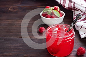 Homemade raspberry jam in a glass jar and fresh raspberries with mint on a wooden rustic background. Copy space
