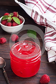 Homemade raspberry jam in a glass jar and fresh raspberries with mint on a wooden rustic background. Copy space