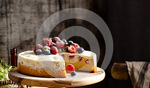 Homemade raspberry sliced biscuit cake with white cream and berries on top on wooden cake stand