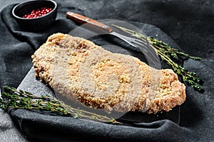 Homemade raw breaded German Weiner Schnitzel. Black background. Top view