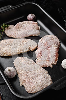 Homemade raw breaded German Weiner Schnitzel set, on black wooden table background