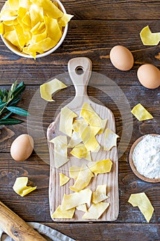 Homemade raw pasta Maltagliati on cutting board with ingredients on wooden background. Top view