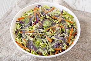 Homemade Raw Shredded Broccoli Slaw in a white bowl on a white wooden background, side view. Close-up