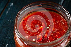 Homemade red hot chili pepper sauce in a glass bowl on a dark wooden background