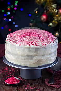 Homemade red velvet cake with cream cheese frosting and red sugar decoration, low key photo with boke lights and christmas