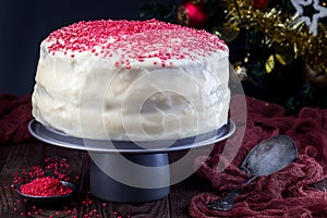 Homemade red velvet cake with cream cheese frosting and red sugar decoration, low key photo with christmas decoration on