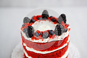 Homemade red velvet cake decorated with berries on a light wooden background