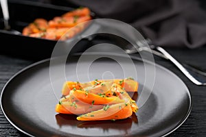 Homemade roasted honey glazed baby carrots with thyme, in a ceramic bowl on a dark wooden table, close up