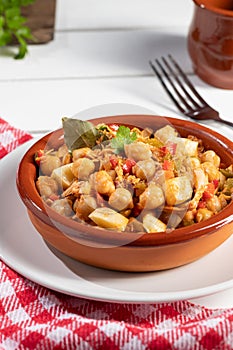 Homemade Ropa vieja, typical Canarian dish of chickpeas stew in earthenware casserole on white table. Vertical format photo