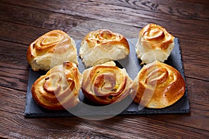 Homemade rose buns on wooden cutting board over rustic vintage background, close-up, shallow depth of field