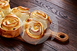 Homemade rose buns on wooden cutting board over rustic vintage background, close-up, shallow depth of field
