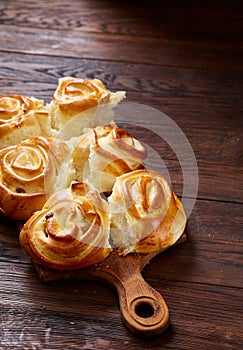 Homemade rose buns on wooden cutting board over rustic vintage background, close-up, shallow depth of field