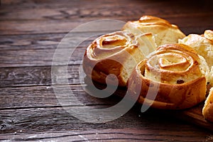 Homemade rose buns on wooden cutting board over rustic vintage background, close-up, shallow depth of field