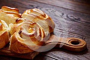 Homemade rose buns on wooden cutting board over rustic vintage background, close-up, shallow depth of field