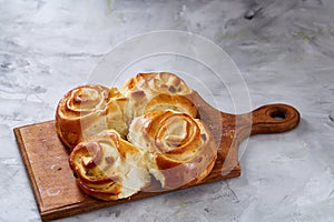 Homemade rose buns on wooden cutting board over white textured background, close-up, shallow depth of field