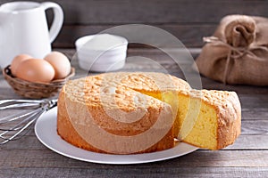 Homemade round sponge cake or chiffon cake on white plate so soft and delicious with ingredients: eggs, flour, milk on wood table photo
