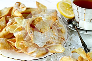 Homemade russian traditional cookies Brushwood on a white plate close-up, selective fokus. Rear cup of tea, slice lemon, sugar