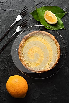 Homemade rustic dessert. Tasty open lemon pie with wholegrain crust served with raw lemons and forks on black background copy