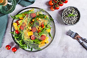 Homemade salad of orange, cherry tomatoes and arugula on a plate on the table top view