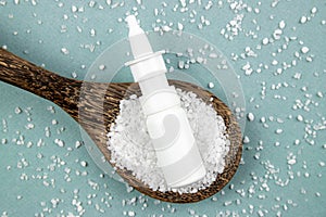 Homemade saline nasal spray bottle on scattered sea salt grains and wood spoon.