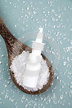 Homemade saline nasal spray bottle on scattered sea salt grains and wood spoon.