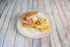 Homemade sandwich with fried egg, bacon and slices of cheddar cheese, lettuce and chicken meat, garnish of homemade fried potatoes