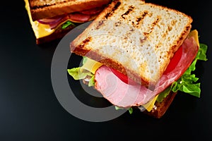 Homemade sandwich with lettuce and ham on a black background, close up