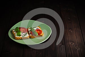 Homemade sandwich made of toast bread, cream cheese, tomatoes, basilico and rucola on a wooden background