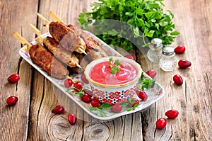Homemade sauce dogberry with meat kebabs on wooden skewers.